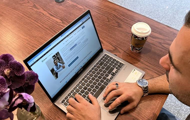 Hamed Farhadian working on a laptop at a wooden table, next to a coffee cup and an orchid.