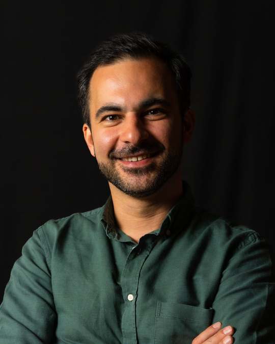 Hamed Farhadian, SEO-Experte aus Hamburg, im grünen Hemd vor dunklem Hintergrund.