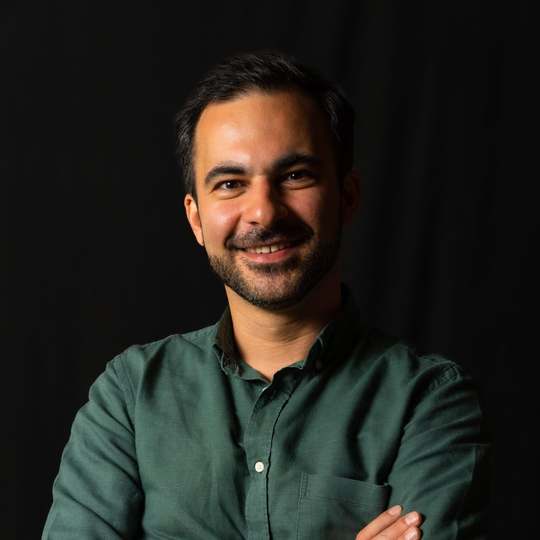 Hamed Farhadian, SEO-Experte aus Hamburg, im grünen Hemd vor dunklem Hintergrund.