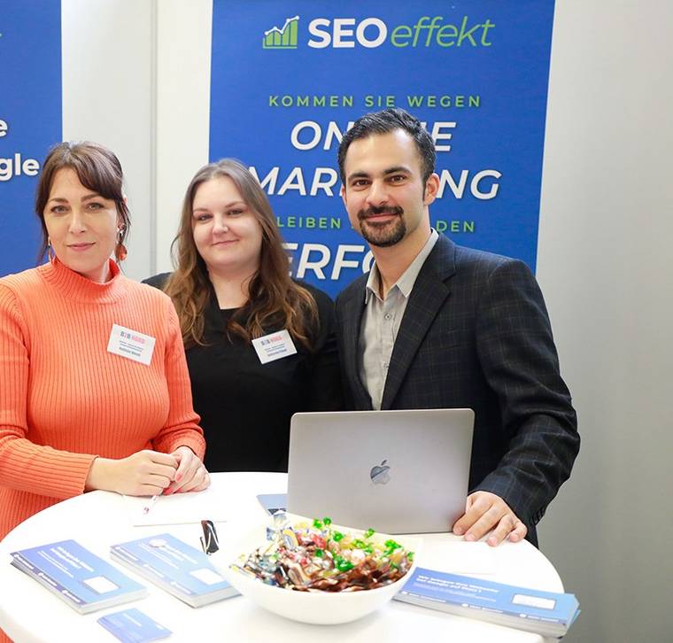 Hamed Farhadian with two SEOeffekt colleagues at a trade fair stand, a laptop and brochures in front of them