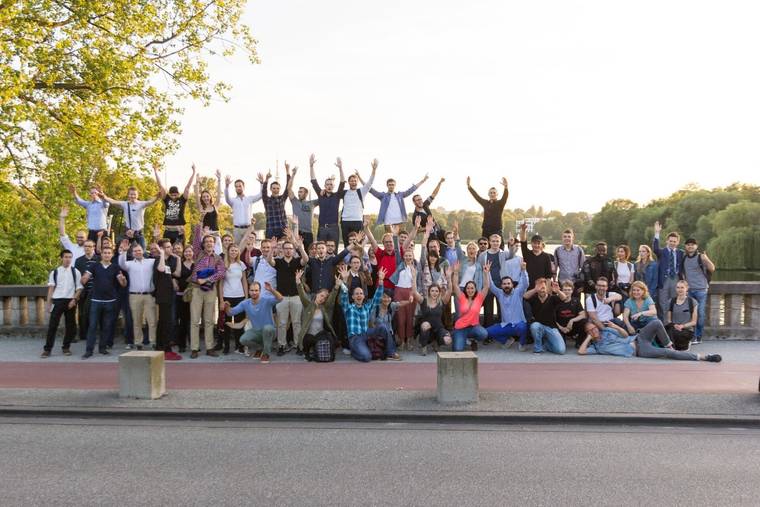 Around 50 Startup Walk & Talk participants pose for a group photo on a bridge by the Alster lake, many with their arms raised
