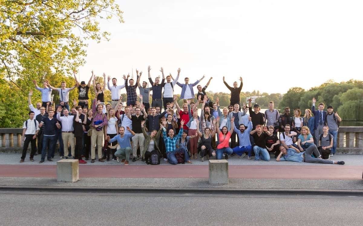 Group photo of Walk & Talk Hamburg in a park by the Alster, many participants cheering with raised arms